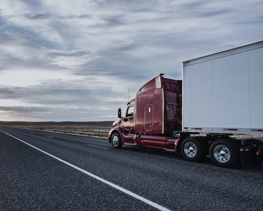 A commercial semi truck traveling on a highway under a cloudy sky