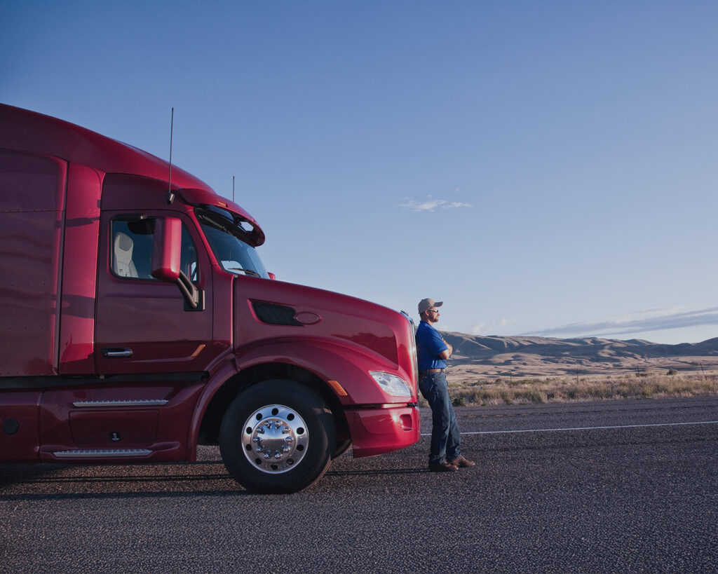 A man standing beside a red semi truck parked on a rural road